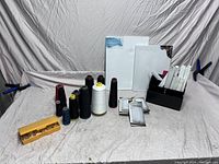 Full lot showing canvases, thread spools, art markers, and plastic clips on cloth backdrop held by clamps