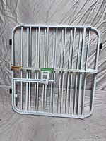 White metal baby gate with vertical bars and small pet door leaning against fabric backdrop
