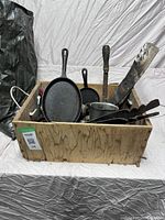 Wooden box showing cast iron pans, lawnmower blades, sledgehammer heads among other metal items