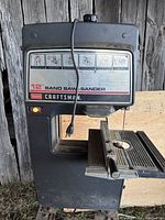Front view of the black Craftsman 12-inch band saw/sander with power cord hanging and instructional decal on front.
