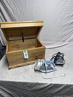 Hardwood box and two electric irons with cords on a neutral background.