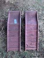 Top down photo of two metal car ramps on grass showing rust and dirt.