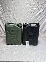 Front view of two military surplus water jugs, one green and one black, placed side by side on a white fabric backdrop.