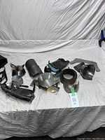 Photo of various medieval-style metal armour parts laid on white cloth background showing 10 separate pieces including gauntlet, forearm guards, knee or elbow plates, and neck plate.
