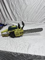 Side view of yellow and green Pioneer 1074 chainsaw on white wrinkled sheet background.