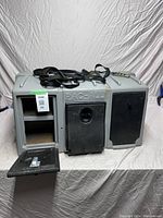 Front angle showing open left compartment with shelving, closed center and right compartments with black doors, and straps on top.