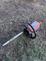 Photo of the full chainsaw lying on grass with visible blade and brand name on the bar.