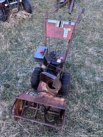 Photo showing full view of rusted Tecumseh snow blower on grass, with large wheels and front auger housing, engine visible on top.