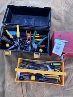 Open black plastic toolbox showing multiple hand tools including pliers and screwdrivers, small tools in a two-tier yellow tray inside.