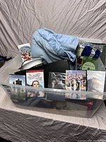 Plastic storage tote with visible DVD cases, hockey jersey, and sailor's hat.