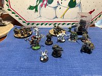 Overview of all 12 Warhammer 40K character miniatures displayed on a blue cloth with a snowman table runner background. Mixed range of painting and base styles visible.