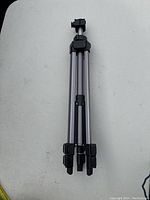 Full view of folded camera tripod showing silver tubular legs with black plastic locks.