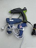 Three electric glue guns grouped together on a light surface, showing different sizes and colors.