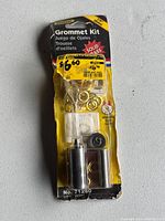 Front view of new sealed General Solid Brass Grommet Kit 1/4 inch (6 mm) showing brass grommets, setting tool, and fabric piece in packaging with yellow price sticker.