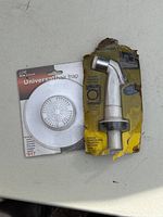 Photo showing kitchen sink sprayer and universal hair trap in original packaging on a table.