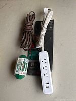Three power-related items on a surface: brown extension cord, white braided power cord, and power strip on original packaging with Cordsafe label visible.