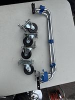 Overview of the four swivel plate casters with rubber wheels and the two chrome-plated tubular metal handle bars laid out on a flat surface.