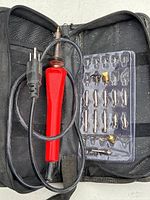 Full view of soldering iron with red handle, power cord, and tips inside black zippered case.