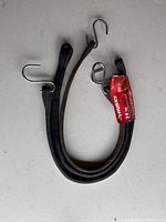 Two black rubber straps with metal S-hooks on ends placed on white surface. Each strap has a red Husky brand tag stating length 24 in.
