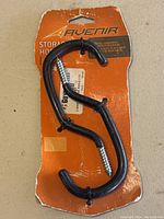 Front view of two black metal S-shaped storage hooks on orange backing card labeled 'Avenir Storage Hooks'.