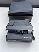 Polaroid Spectra System SE camera front with flash, lens, and branding visible, included black case behind camera