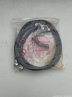 Coiled black washing machine water hose in original plastic packaging with printed safety warnings.