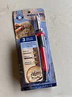Full pack showing wood burning tool and packaging with artistic corner branding and wood-burned art examples.
