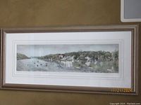 Full framed panoramic print showing river, boats, and village scene under glass with beige frame.