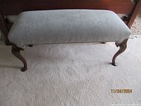 Front view of bench showing upholstered gray seat and carved wooden legs.