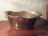 Vintage brass planter with wavy rim and side handles on wood surface