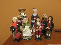 Group photo of 7 Byers Carolers figurines posed on a wooden table showing details and clothing styles.