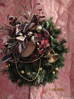 Full view front of the Christmas wreath showing ribbon bows, metallic ornaments, pine cones, faux berries and greenery on a pink backdrop.