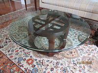 Full view of round coffee table on patterned rug showing glass top and wooden base