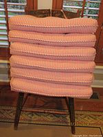 Stack of six red and white gingham patterned seat cushions on a wooden chair.