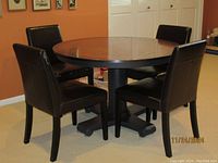 Wide angle view of round dining table with four brown leather chairs around it, set in a room with tan walls.
