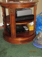 Side view of Ethan Allen round library table showing double shelves with carved floral detailing on the vertical supports and rich wood finish.