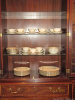 Full view of china displayed in a wooden cabinet with upper shelf holding cups and saucers, middle and lower shelves holding plates and bowls.