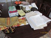 Table display showing assorted folded linens including patterned and solid table covers, towels and two brown bee themed bathroom accessories.