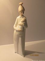 Front view of Lladro figurine showing standing mother holding child wrapped in blanket, cream and beige tones, 8.5 inches tall.