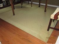 Full view of beige Masland area rug installed on hardwood floor under dining table and chairs.