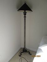 Full view of the metal pole floor lamp showing height, triangular metal shade and ornate sturdy base with curled feet.
