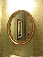 Full view of oval mirror hanging on wall showing gold-tone gilt frame and reflection.