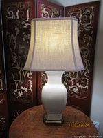 Front view of one lamp showing white ceramic body with hexagonal brass base and beige fabric shade.
