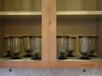 Eight amber tinted, hand blown glass rummers displayed on a shelf, showing overall set condition and quantity.