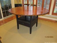 Front view of round tabletop in horizontal position showing wood finish and black base with drawer