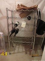 Full view of the chrome metal wine rack showing five shelves for bottle storage with some bottles and paper on the top shelf