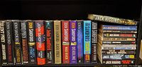 Shelf of John Sandford hardcover novels mostly with black dust jackets, lined up side by side, showing titles clearly.