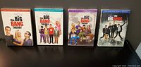 Four DVD cases of The Big Bang Theory seasons 1 through 4 lined up on a black surface.