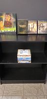 The Lord of the Rings Official Movie Guide, three Lord of the Rings DVDs in cases, and ten other assorted DVDs stacked beneath on a black shelf.