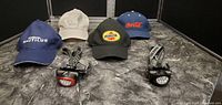 Four ball caps and two LED flashlight headlamps arranged on a dark, marbled surface, showing the front logos and designs of the caps and the light on the headlamps.